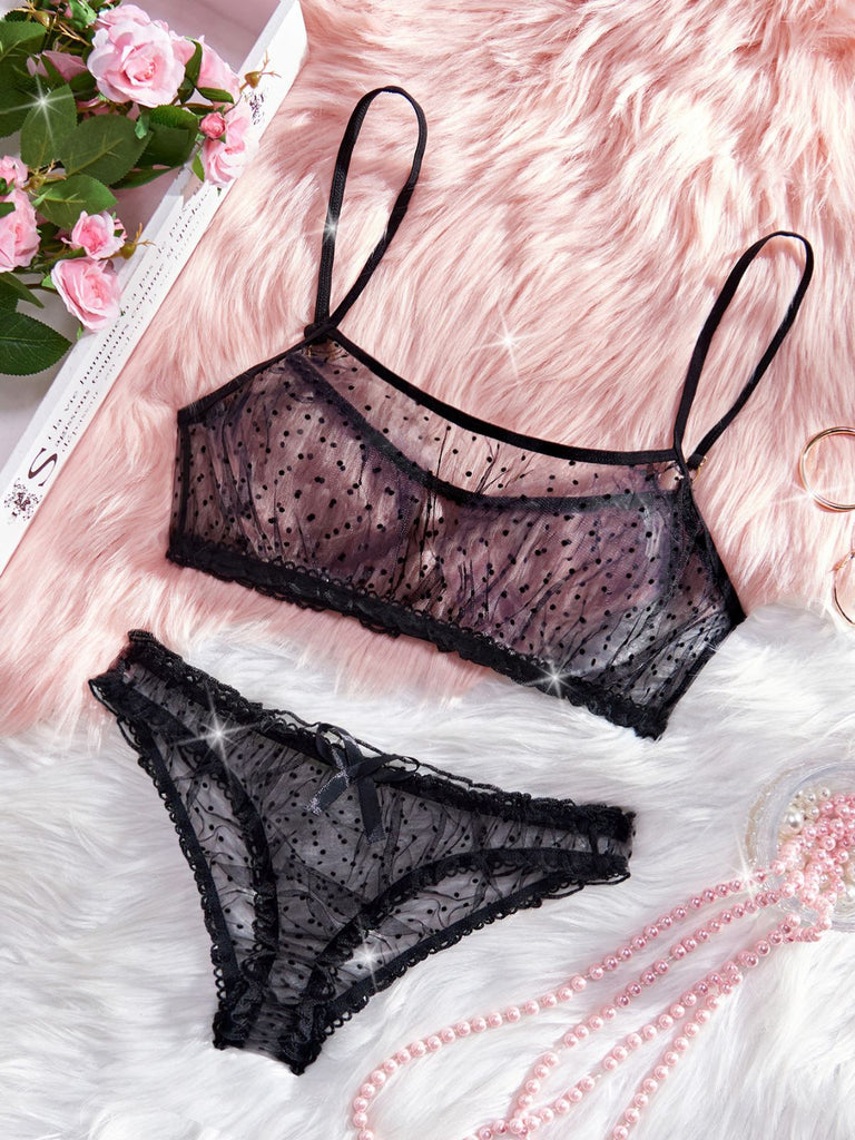 Black lace lingerie set on a soft pink surface with flowers in the corner.