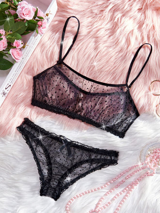 Black lace lingerie set on a soft pink surface with flowers in the corner.