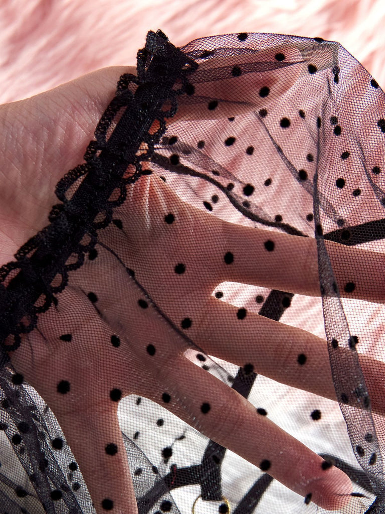 Hand wearing a black polka dot sleepwear on a pink background