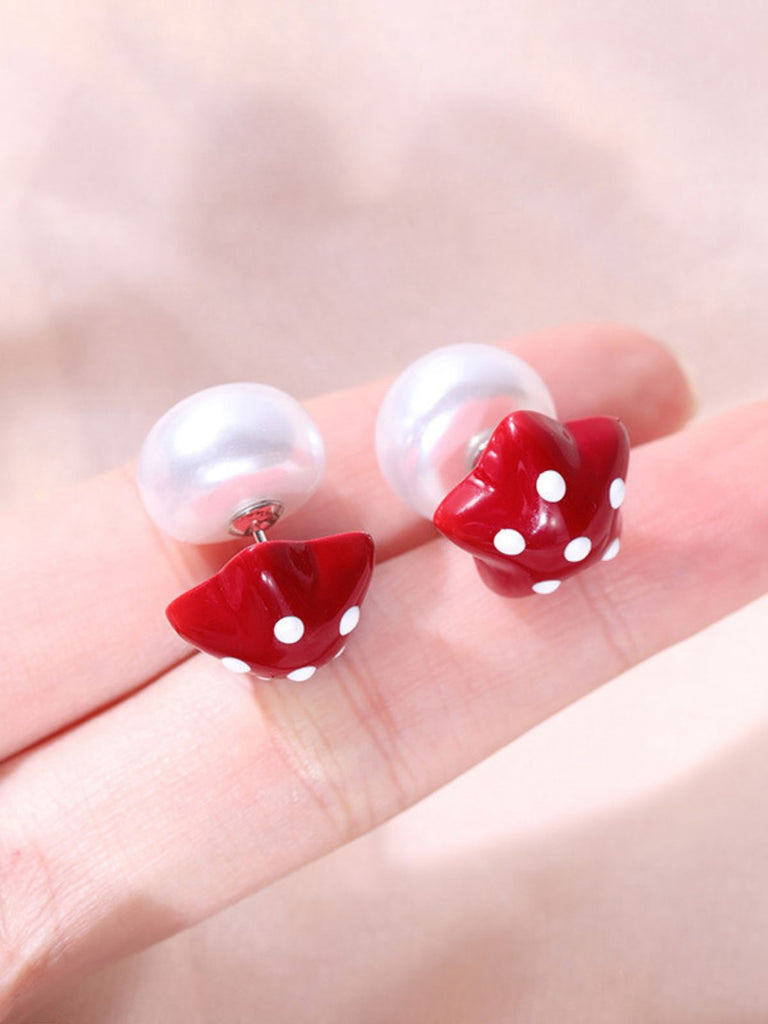 Pair of earrings with white pearls and red strawberry-shaped pendants on a hand.