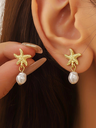 Gold starfish earrings with pearl drops worn by a person.