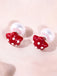 Pair of earrings with red mushroom-shaped studs on a light pink background