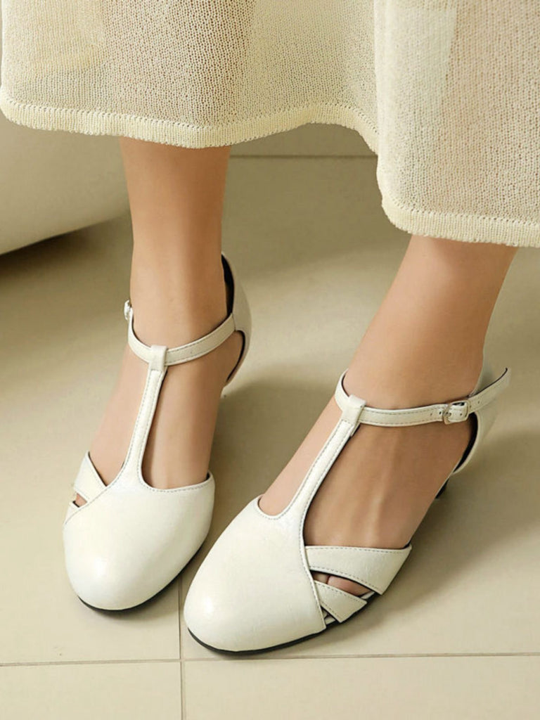 White sandals worn with a light-colored skirt on a neutral floor.