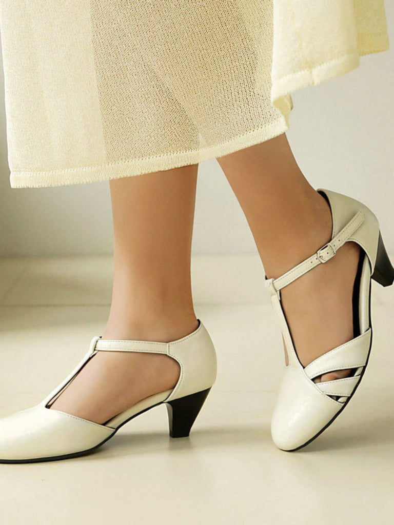 White medium-heeled shoes worn with a light-colored skirt on a neutral background