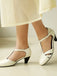White medium-heeled shoes worn with a light-colored skirt on a neutral background