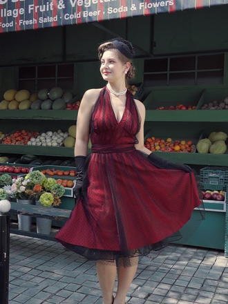 A burgundy 1950s style swing dress with a black polka dot mesh overlay, featuring a halter neck and sleeveless design, shown with a fashion illustration.