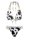 A triangle bikini set featuring a black and white cow print with decorative gold chain-link straps on both the top and high-cut bottoms.
