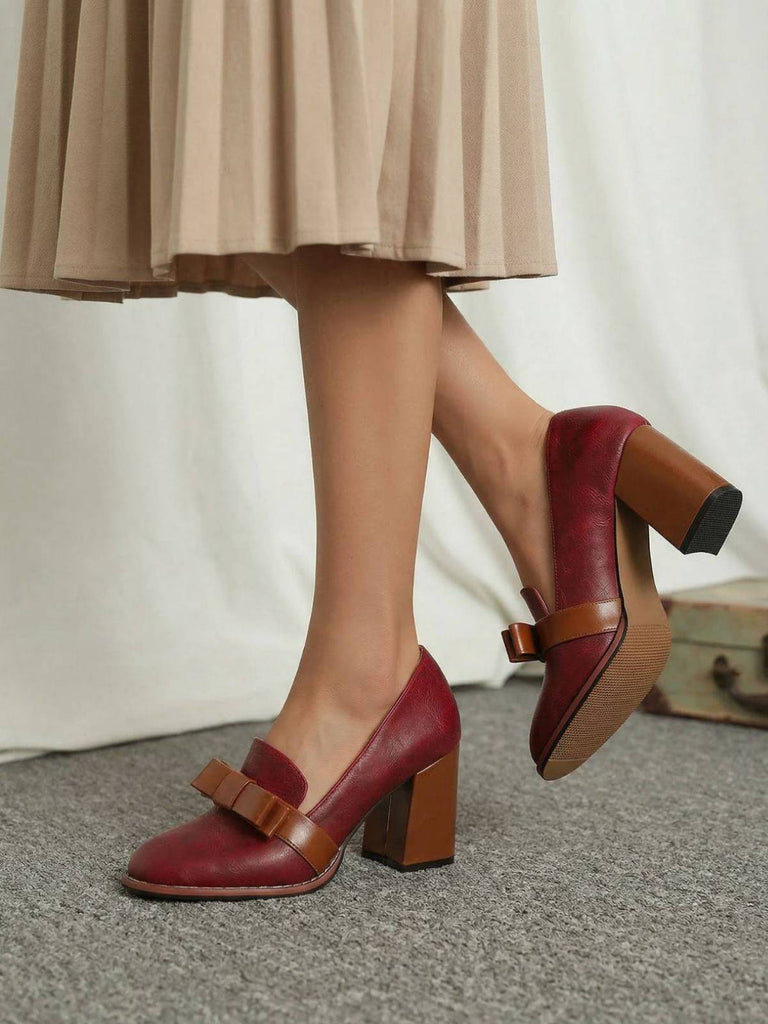Red high-heeled shoes with brown soles worn by a person in a beige skirt.