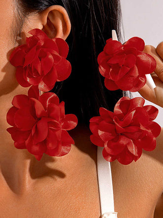 A model wearing large, bold red fabric earrings featuring a cluster of four 3D floral petals for a dramatic look.