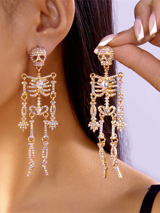 A pair of elaborate gold-tone drop earrings shaped like skeletons, fully encrusted with shimmering clear and iridescent rhinestones.