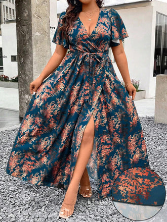 A woman wearing a teal wrap-style maxi dress featuring a rust-colored floral print, a deep V-neckline, flutter sleeves, and a high leg slit.