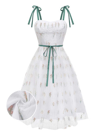 A delicate white tulle A-line dress featuring dainty embroidered wildflowers, dark green velvet tie-straps, and a matching velvet waist ribbon.